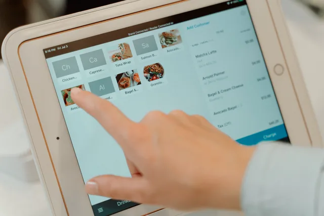 Finger tapping on a tablet screen to select food items in a restaurant setting. POS implementation and training